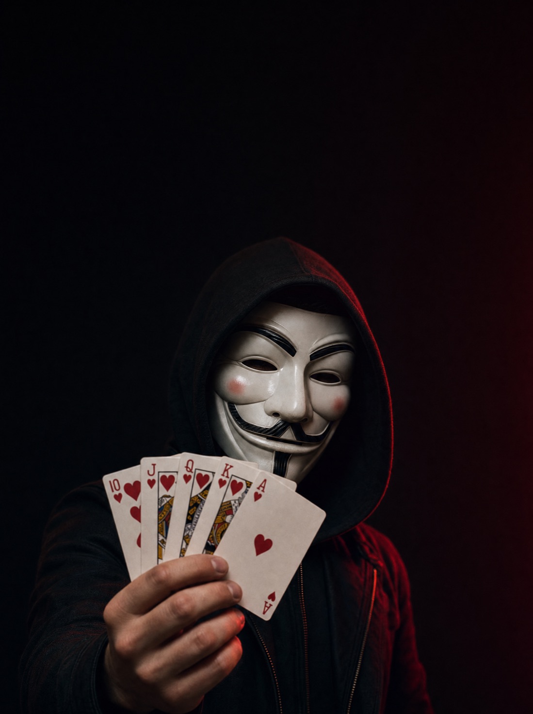 A masked figure in a hood holding a Royal Flush in hearts — the Ten, Jack, Queen, King and Ace